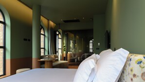 A hotel room with a large bed, a sitting area with a table, and large windows providing natural light. - BHB Boutique House (Macedo de Cavaleiros)
