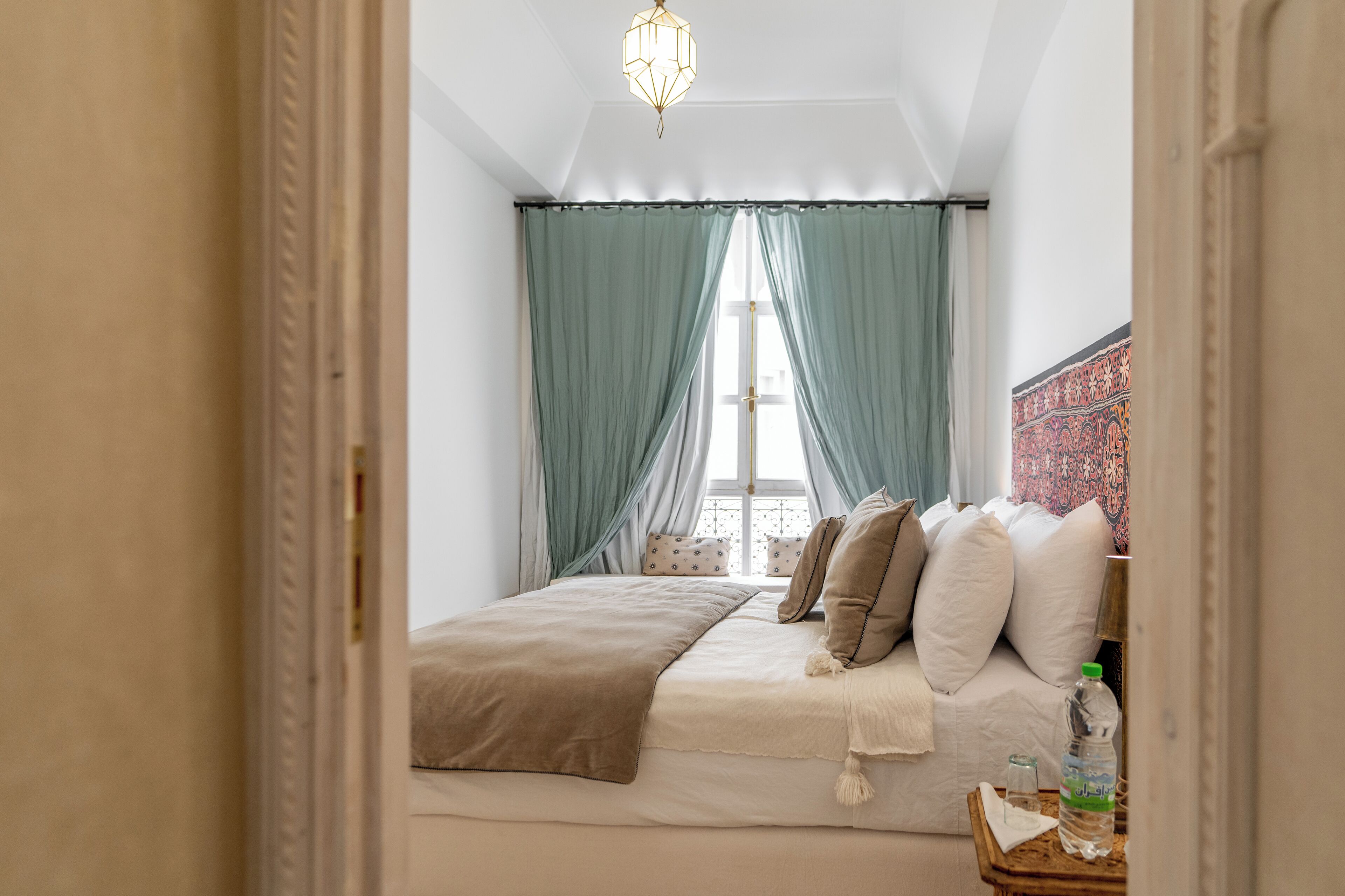 A bedroom with a bed, curtains, a hanging light fixture, and a window.