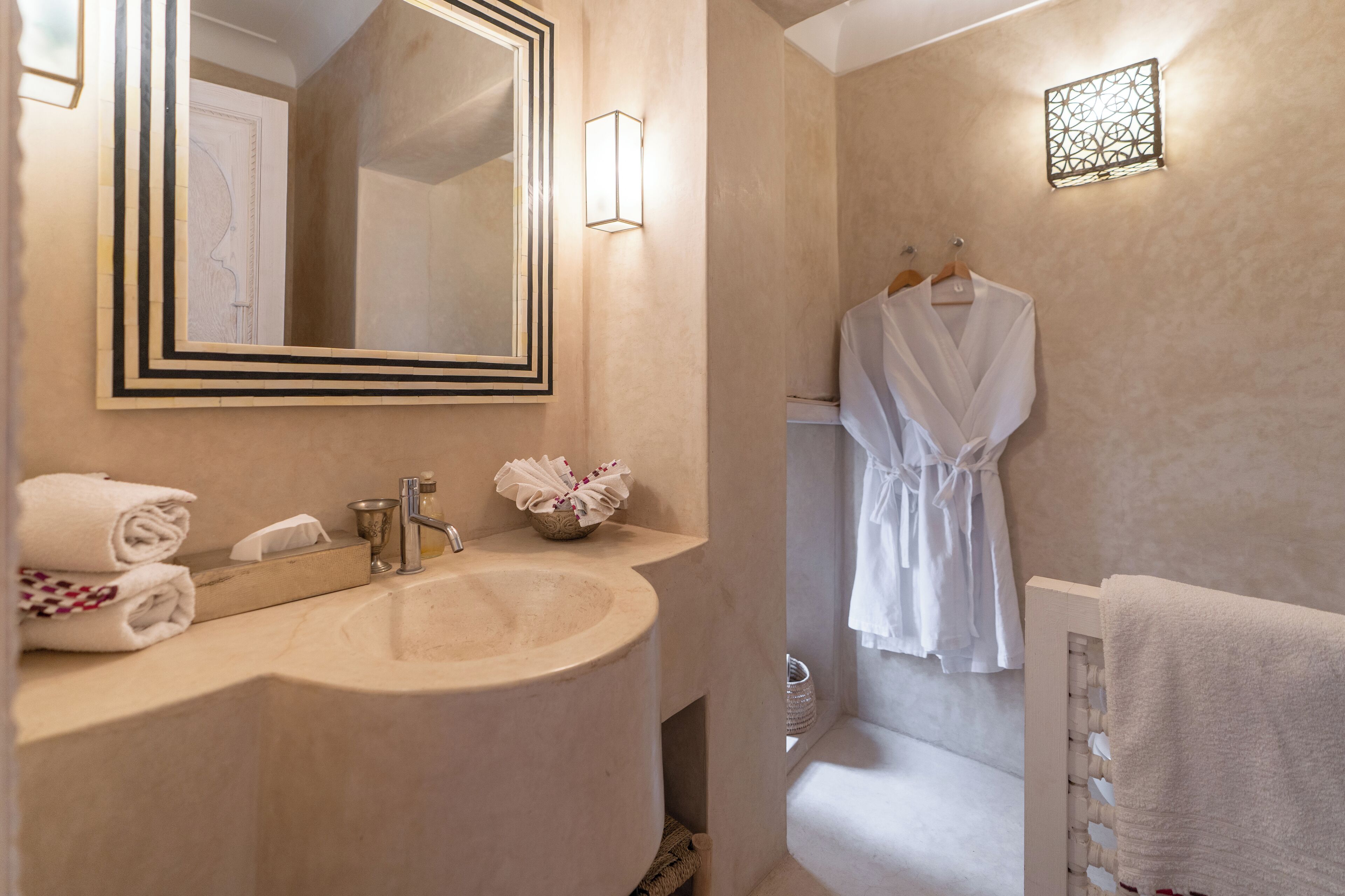 A bathroom with a large mirror, a sink, and a robe hanging on the wall.