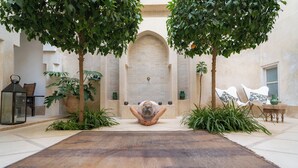 Ein Innenhof mit einer zentralen Meditationsfläche, umgeben von Topfpflanzen und einer großen Matte.
