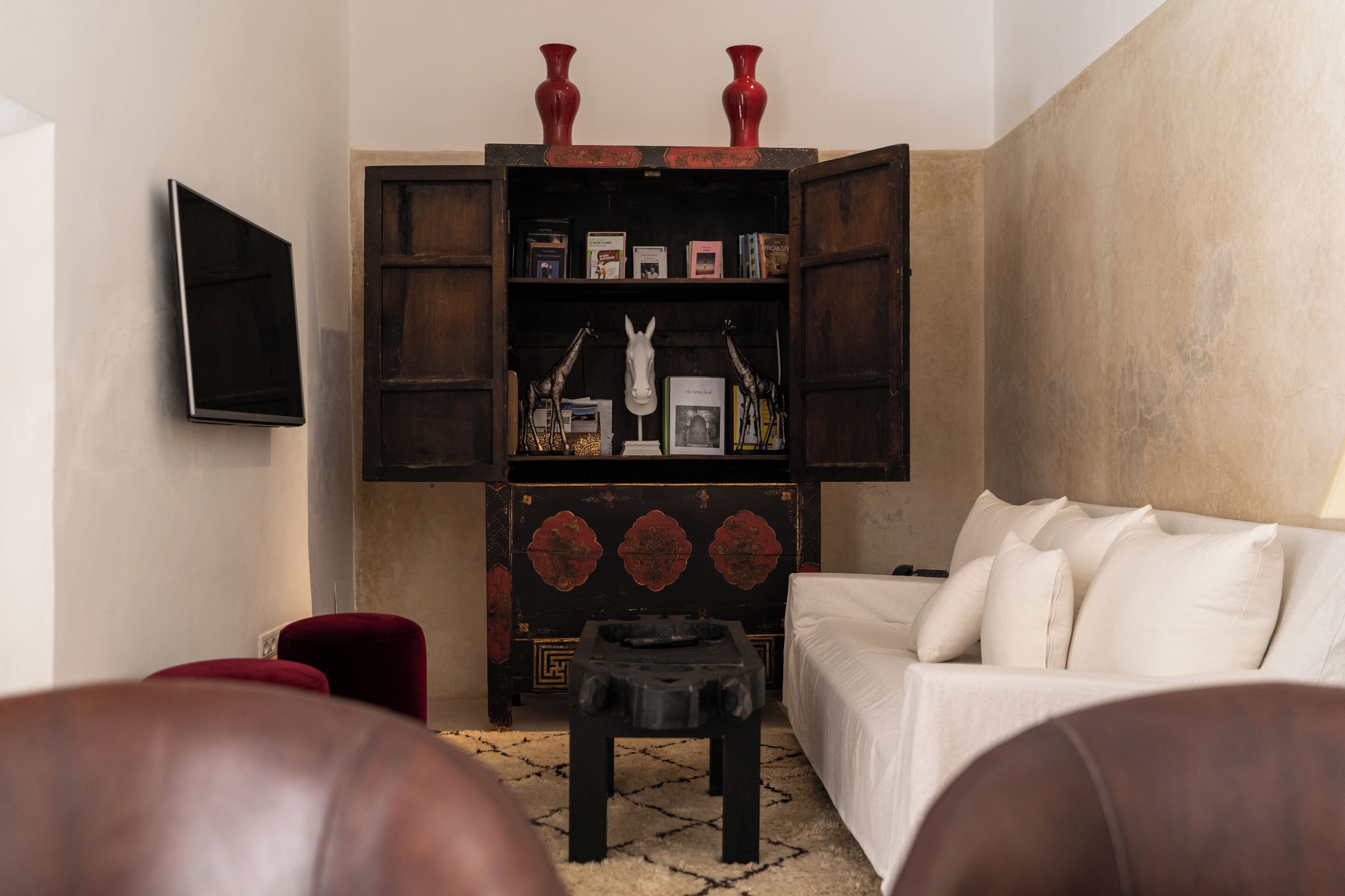 Una sala de estar con un sofá blanco, un reposapiés rojo, una mesa de centro negra y una estantería de madera con adornos.