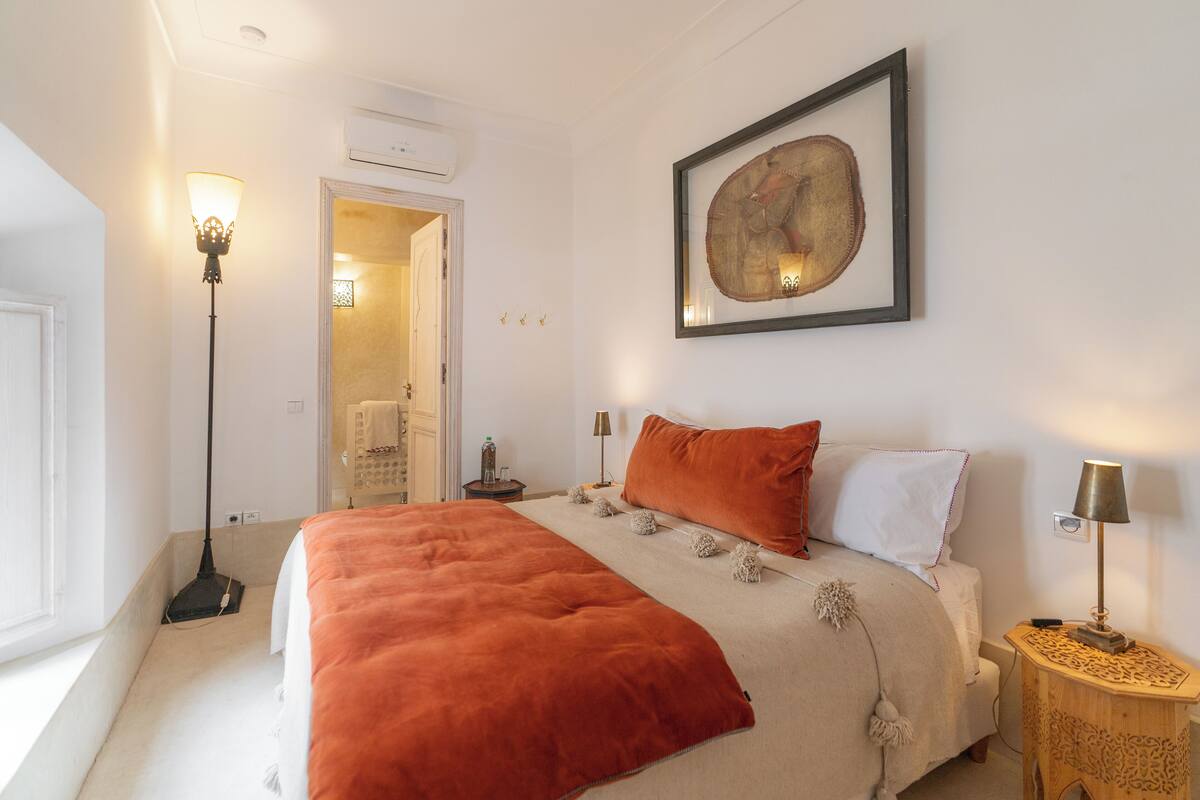 A bedroom with a large bed, a floor lamp, a bedside table, and a framed artwork on the wall.