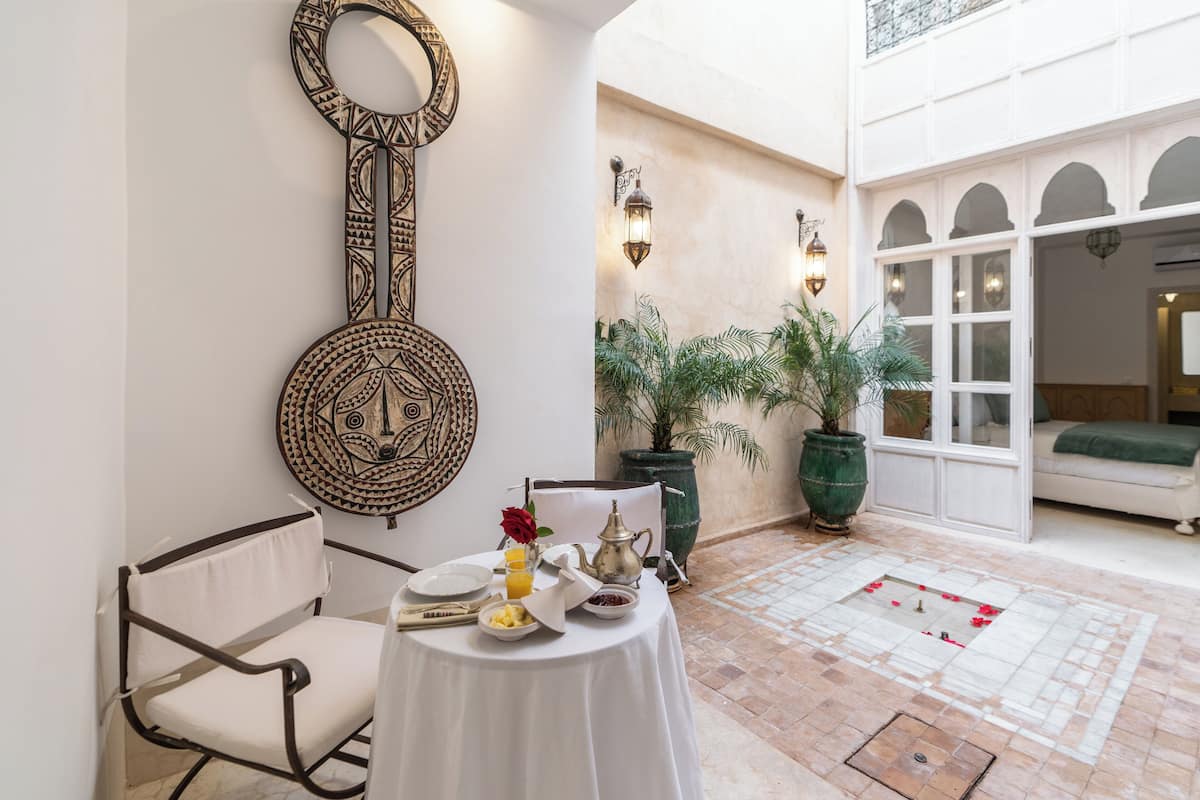 A dining area with a table set for breakfast, a decorative wall piece, and potted plants.