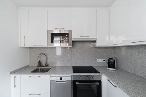 A modern kitchen with white cabinets, a stainless steel microwave, a dishwasher, an oven, and a coffee maker. - Penthouse Center (Vigo)