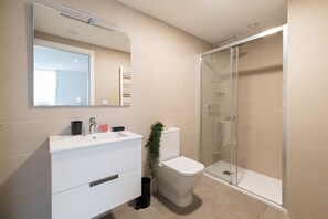 Un baño moderno con tocador blanco, inodoro y ducha con mampara de vidrio.