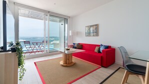 Ett modernt vardagsrum med en röd soffa, ett soffbord i glas och utsikt över havet genom stora skjutdörrar.