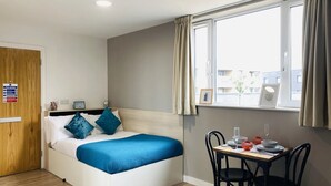 Ein Schlafzimmer mit Bett, Nachttisch, Fenster mit Vorhängen, einer Holztür und einem Brandschutzschild.