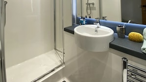 Ein modernes Badezimmer mit einer gläsernen Dusche, einem weißen Waschbecken und einem Spiegel darüber.