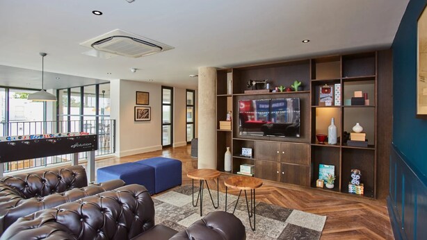 Ein modernes Wohnzimmer mit Billardtisch, Ledersofas, Fernseher und Holzboden.