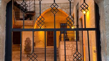 An arched doorway with a metal gate, leading to a staircase and a room with a stone wall and a wooden door.