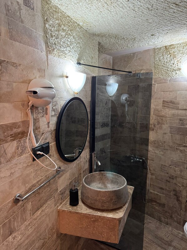 A modern bathroom with a stone sink, a round mirror, and a glass-enclosed shower.