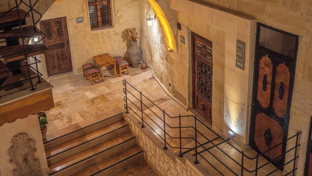 A stone staircase leading to a second floor with a wooden railing, a small table with chairs, and a wooden door with a decorative panel. - Colina Stone House (Ürgüp)