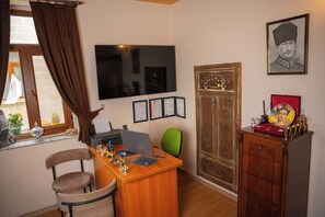 A room with a wooden desk, a green chair, a television mounted on the wall, and a large wooden cabinet. - Colina Stone House (Ürgüp)