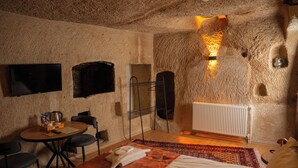 A cozy room with a bed, a small round table with chairs, a flat-screen TV, and a unique textured wall feature. - Colina Stone House (Ürgüp)