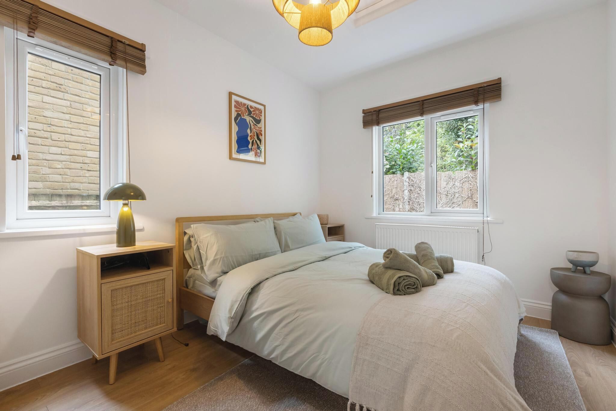 A bedroom with a bed, bedside lamp, bedside table, and a window with blinds.