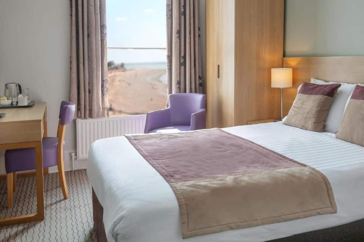 Habitación de hotel con cama, escritorio, silla y vista a la playa.