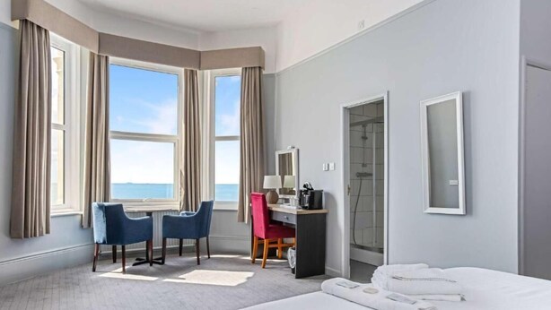 Habitación de hotel con cama, escritorio, dos sillas, lámpara de escritorio, espejo y vista al mar.