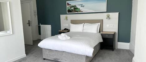 A bedroom with a bed, a nightstand, a bedside table, and a painting on the wall.