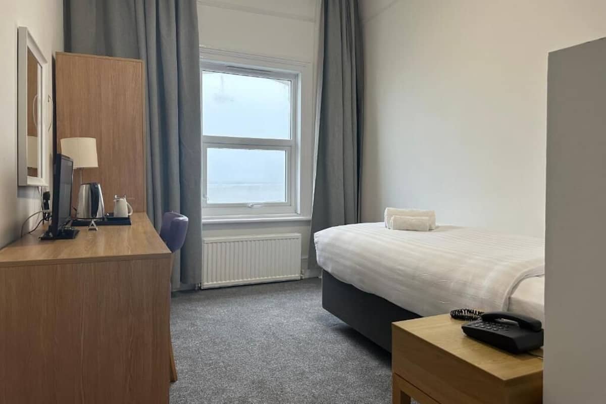 Una habitación de hotel con cama, escritorio con lámpara, teléfono y ventana con cortinas.