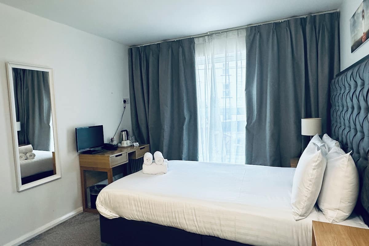 Habitación de hotel con cama, escritorio con ordenador, televisor y ventana con cortinas.