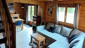 Interior de uma cabana de madeira com sofá, mesa de jantar e lareira a lenha.