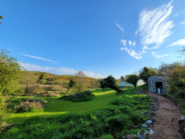 A rural landscape with a stone structure, a grassy path, and a clear blue sky.