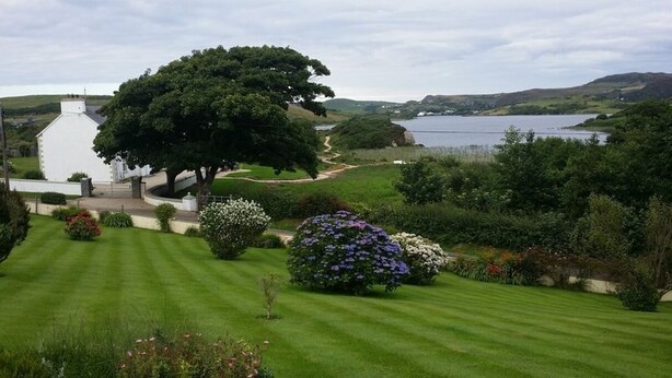 Un jardin bien entretenu, avec un grand arbre, un bâtiment blanc et un lac en arrière-plan.
