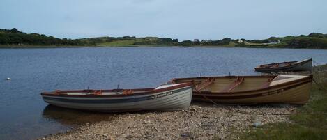 Three rowboats named "Fanad Angling Club" docked on a pebbly shore by a calm lake with a grassy and hilly landscape in the background.