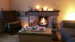 Un salon chaleureux avec une cheminée, un fauteuil confortable, un canapé et une petite table sur laquelle se trouve un plateau de collations.