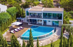 Una moderna casa a due piani con piscina, area salotto esterna e un giardino rigoglioso.