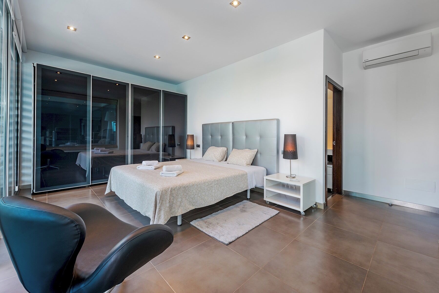 Een moderne slaapkamer met een groot bed, een nachtkastje, een stoel en een glazen scheidingswand.