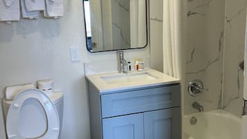 A bathroom with a toilet, sink, mirror, and shower.