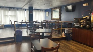 A restaurant with wooden tables and chairs, a bar area, and a television mounted on the wall. - Hilltop Inn & Suites (Yonkers)
