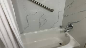 A bathroom with a white bathtub, a handrail, and marble-patterned walls.