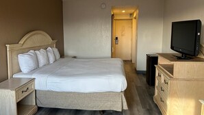 A hotel room with a large bed, a television, a wooden dresser, and a door leading to another room. - Hilltop Inn & Suites (Yonkers)