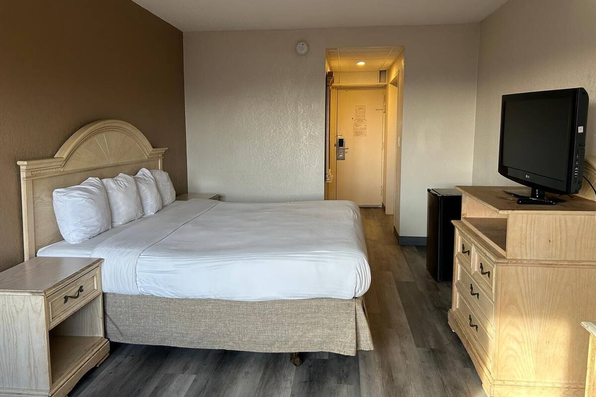 Una habitación de hotel con una cama grande, televisión, cómoda de madera y una puerta que da a otra habitación.