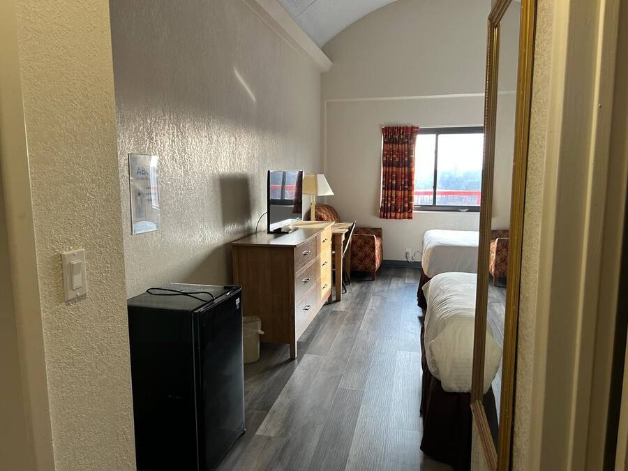 A hotel room with a bed, a desk with a computer, a television, and a window with curtains.
