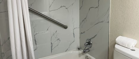 A bathroom with a marble wall, a bathtub, a toilet, and a handrail.