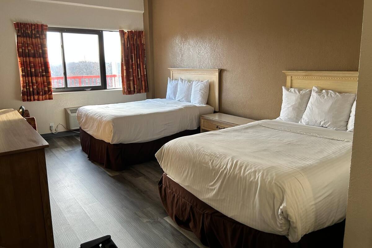 Una habitación de hotel con dos camas, un escritorio y una ventana con cortinas.