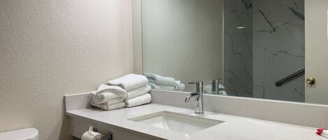 Un baño con un lavamanos blanco, un espejo y una pila de toallas.