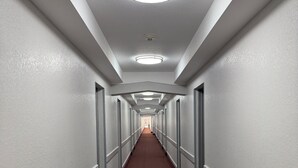 A long, narrow hotel corridor with white walls, a patterned carpet, and recessed lighting. - Hilltop Inn & Suites (Yonkers)