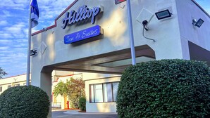 A hotel named 'Hilton' with a sign indicating 'Inn & Suites'. There are two flags on poles, a parking lot, and well-maintained hedges. - Hilltop Inn & Suites (Yonkers)