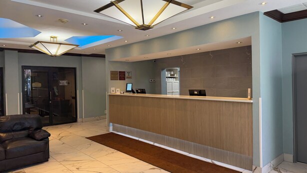 A hotel reception area with a modern design, including a reception desk, seating area, and a ceiling with skylights. - Hilltop Inn & Suites (Yonkers)