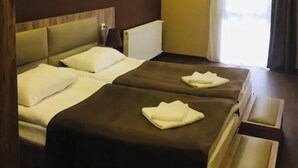 Ein Hotelzimmer mit zwei Betten, einer Holzbalkendecke, einem Fenster mit Vorhängen und einem Nachttisch.