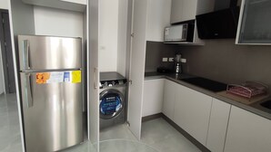 A compact kitchen with a stainless steel refrigerator, a washing machine, a microwave, and a Tesla charging station. - Granda Centeno Luxury Studio (Quito)