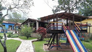 A playground with a slide and climbing structures, surrounded by a stone pathway and greenery. - Hotel Fazenda Aguas VIvas (Pirenópolis)