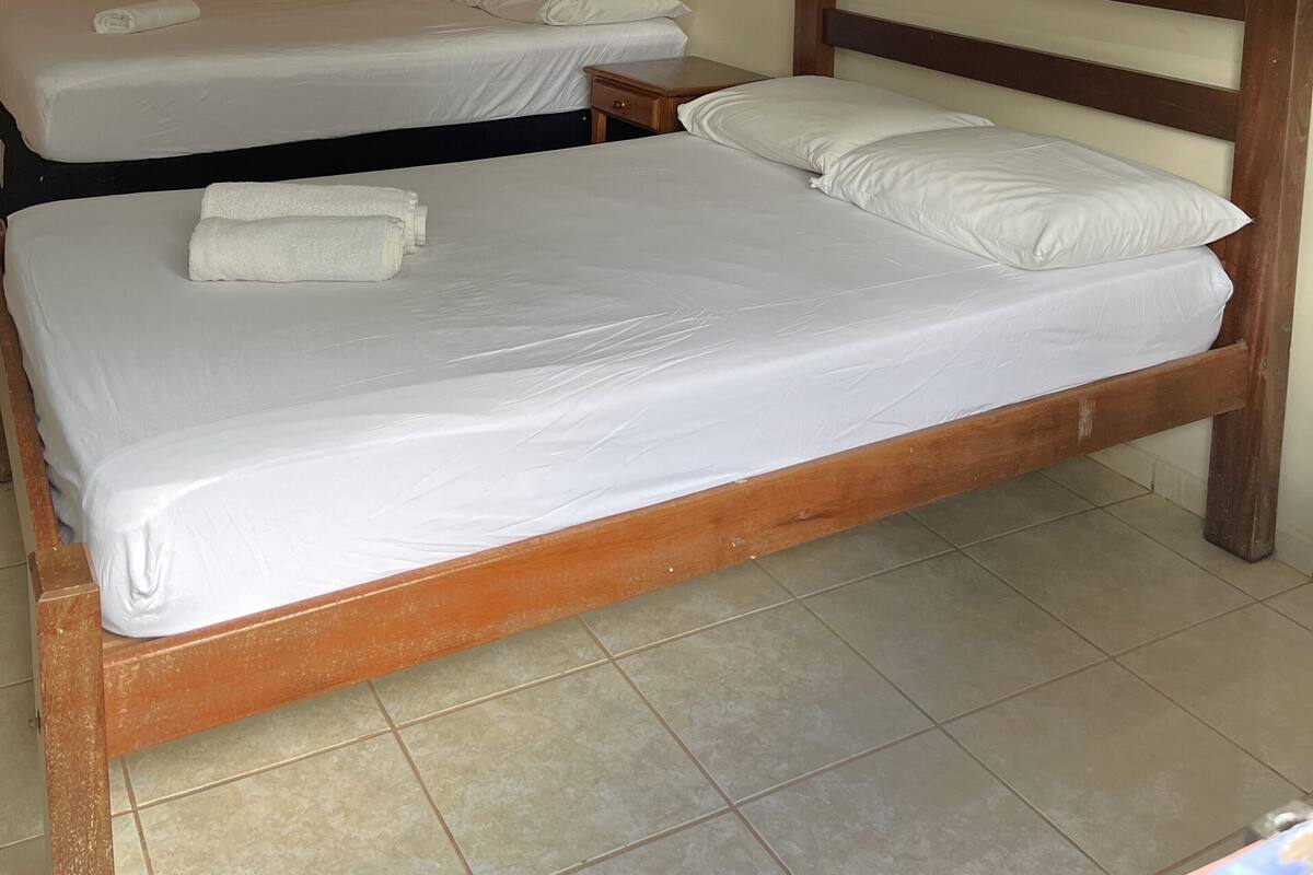 Une chambre dotée de deux lits, chacun avec du linge de lit et des oreillers blancs, des têtes de lit en bois et un sol carrelé.
