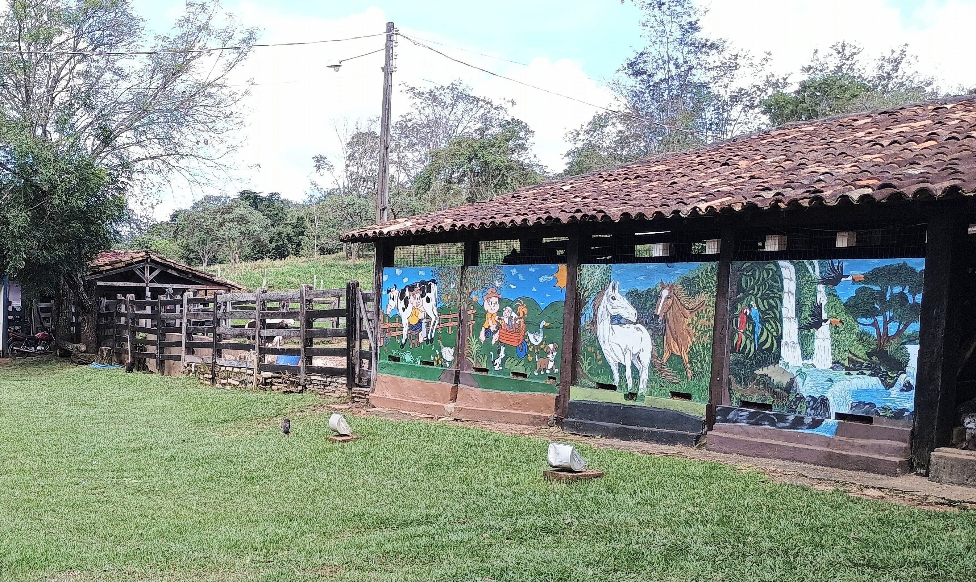 Un edificio rústico con techo de tejas y un mural que muestra animales de granja y paisajes naturales.
