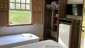 A bedroom with a single bed, a window with wooden shutters, a built-in wardrobe, a small refrigerator, and a television. - Hotel Fazenda Aguas VIvas (Pirenópolis)