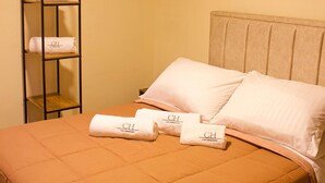 A neatly made bed with a brown quilt, two pillows, and three folded towels with a logo on them. - Spacious 9-bedroom house in wonderful La Calera with WiFi (La Calera)
